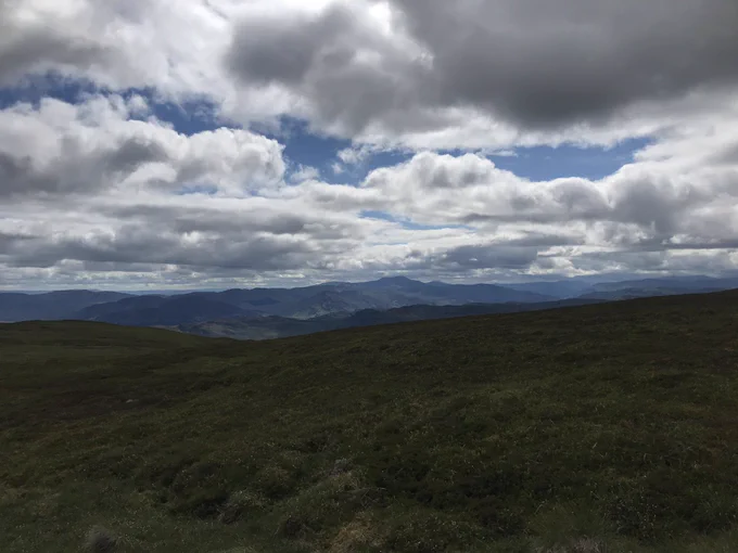 Scottish mountains in the distance, partly cloudy day, very green landscape