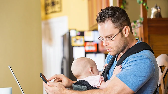 Photograph of a man using his mobile phone while holding his baby