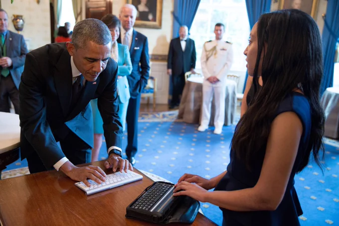 I’m standing at a table reading from a braille computer. President Obama is on the other side of the table typing on a keyboard. Vice President Joe Biden and Valerie Jarrett are standing by watching. Photo by the Obama White House.