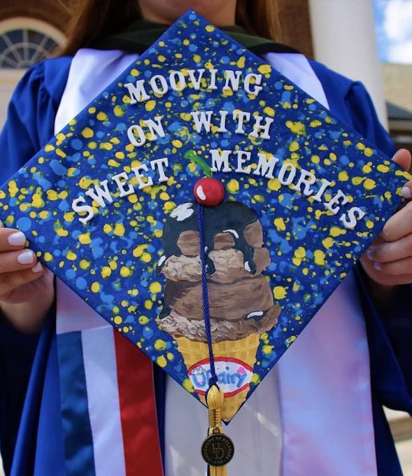 Student poses with graduation cap decorated with UDairy designs and reads Mooving on with Sweet Memories