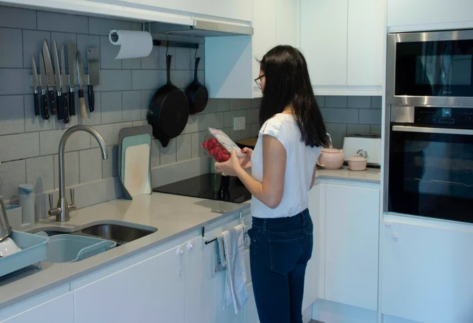 Woman checks packaging for recycling advice, standing in her kitchen