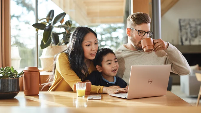 Photograph of a family sat at a kitchen table working on a laptop together