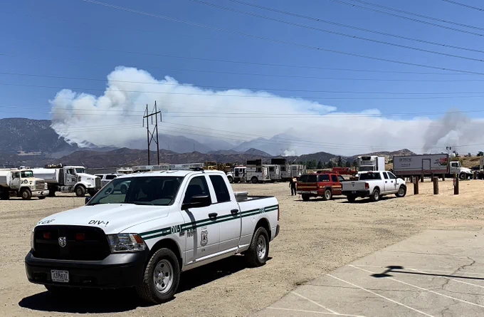 fire personnel vehicles, with a wildfire burning in the background on a mountainside