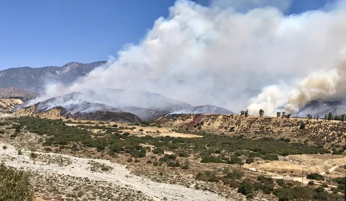 wildfire burning easterly on a lightly vegetated drainage with mountains in the background
