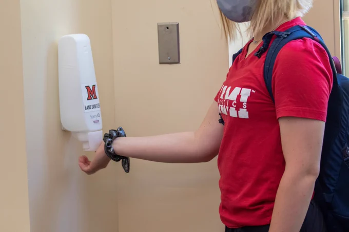 Student reaching for hand sanitizer at a station in Kreger Hall.
