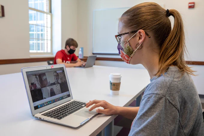 Two students in a large Armstrong Study room, sitting far apart, with masks on.
