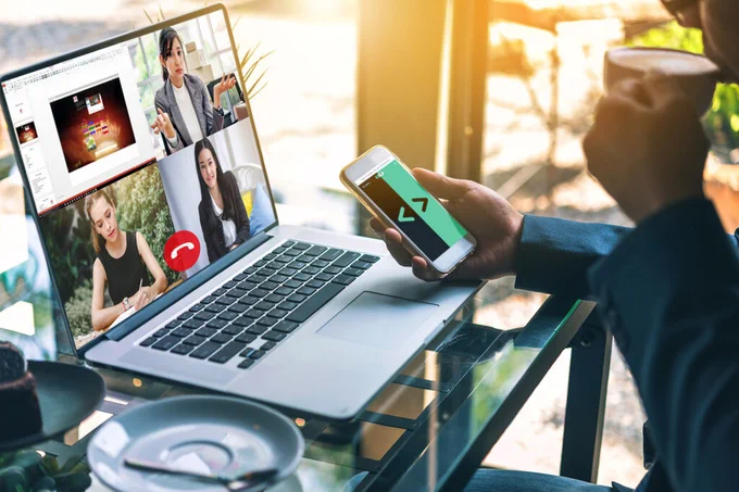 A man drinks coffee in front of his computer having a meeting through skype and using Cliqer application on his iPhone to control a remote presentation.