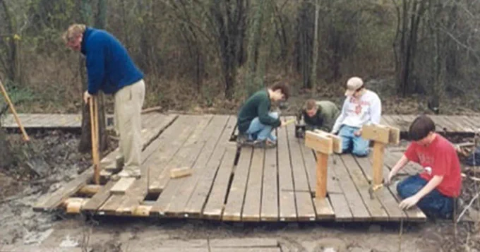 A group of Scouts build a wooden deck in a forest.