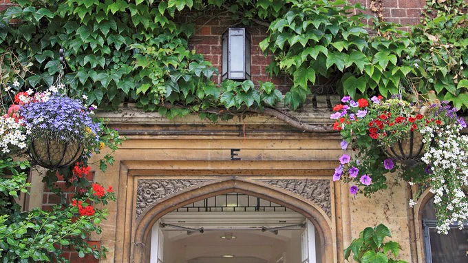 An arch in Selwyn College adorned with ivy and baskets of flowers.
