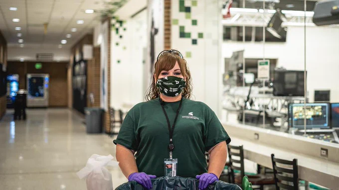 An IPF employee wearing a mask and gloves standing with a garbage can