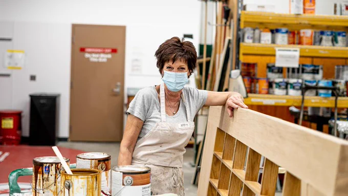 An IPF employee wearing a mask posing and leaning on a wooden structure and paint cans