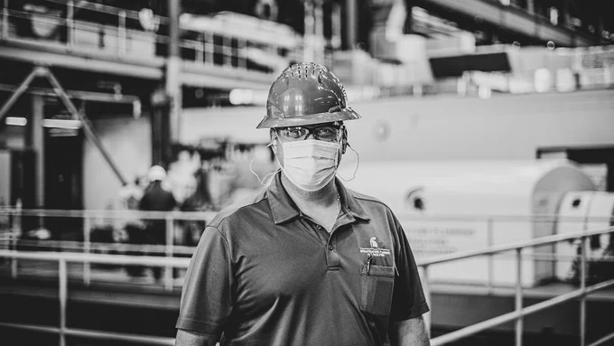 A black and white portrait of an IPF employee wearing a safety hat and mask
