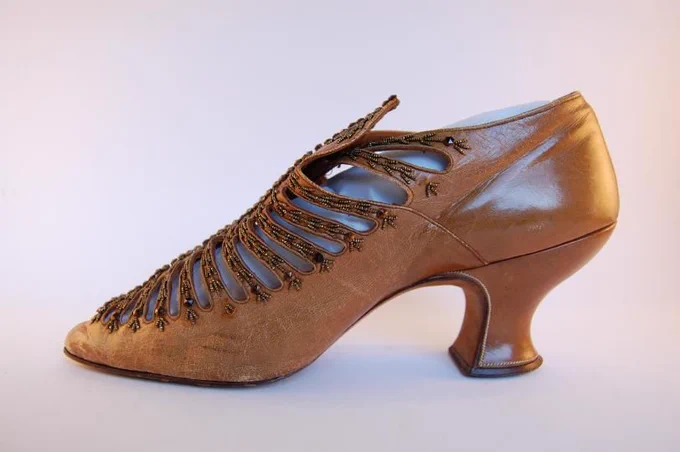 Shiny gold-brown-coloured women's shoe with a curved high heel. The bars on the semi-open top are decorated with gold beadwork.