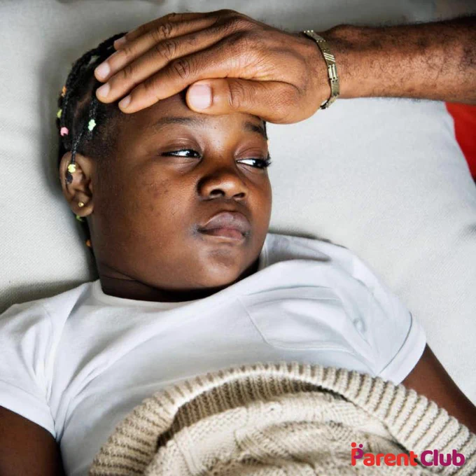 Child in bed looking poorly, with an adult's hand on their forehead
