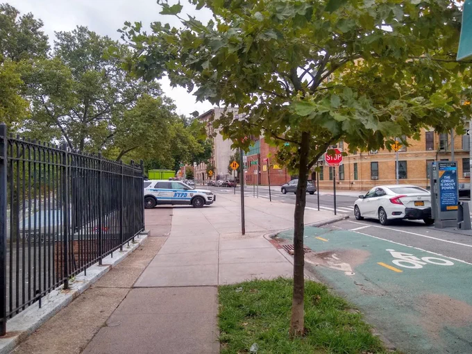 An NYPD SUV is parked on a sidewalk in front of a park.