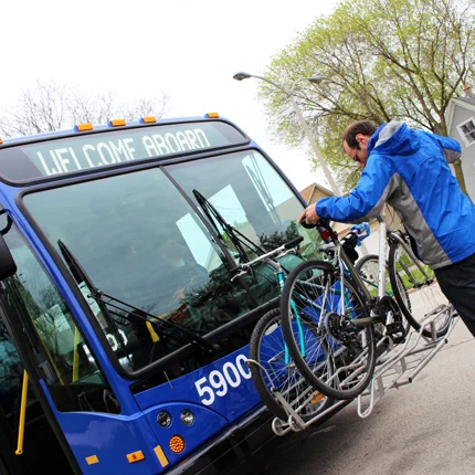 This photo shows a man putting his bike onto the bike rack on the front of a MCTS bus.