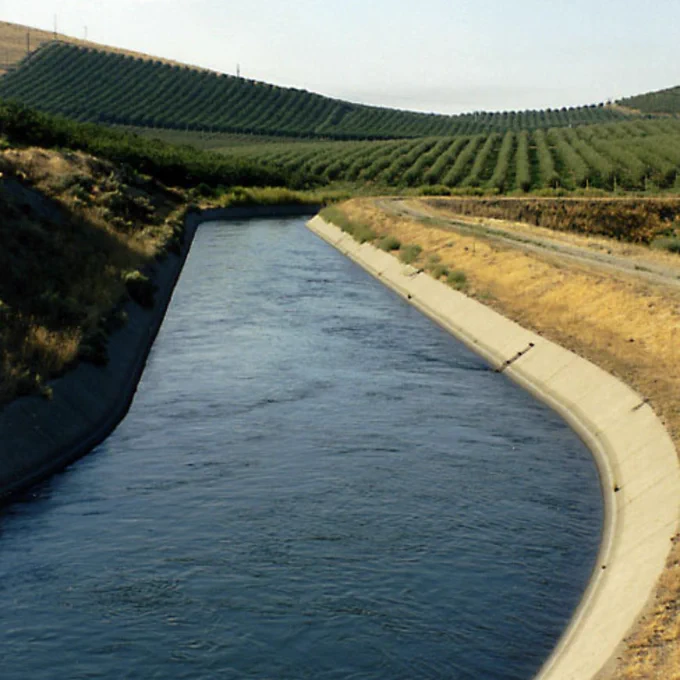 A canal running through the foothills with agricultural fields on each side of it.