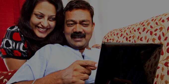 man and woman with brown skin on a couch looking at a laptop 