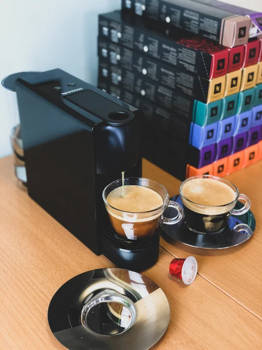 Coffee machine with two glass cups and a stack of Nespresso capsules in the background