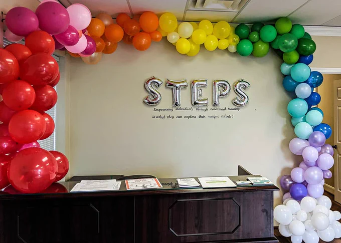 Rainbow balloon arch behind a desk.  Balloons that spell STEPS in the center of the rainbow.