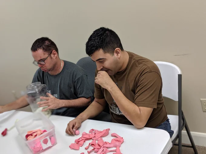 Two young men sorting pink balloons by size and color