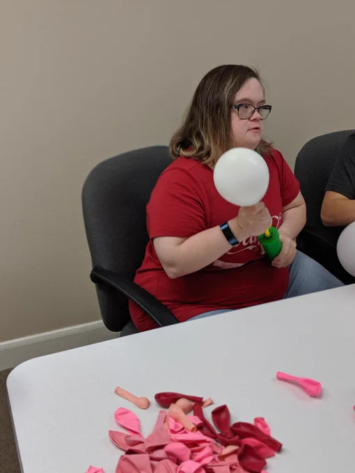 A young woman blowing up a white balloon with a green balloon pump