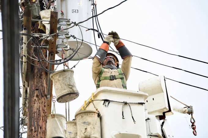 Image of lineworker up in a bucket vehicle repairing a power line. 