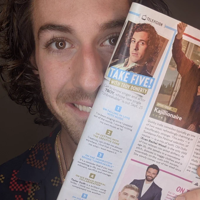 TROY holding his article in Us Weekly