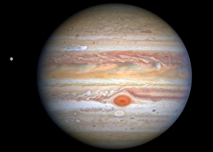 Jupiter image with Great Red Spot visible at lower center and moon Europa in distance.