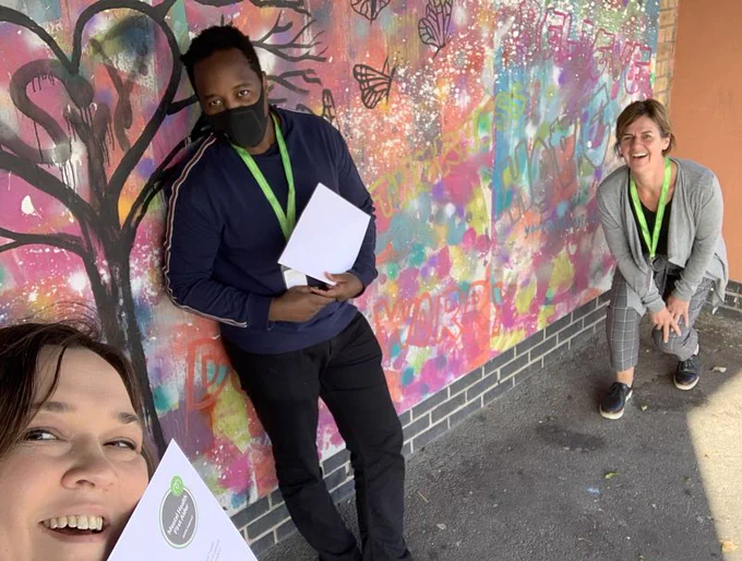 Three Grapevine team members pose against a wall with their Mental Health First Aider certificates.