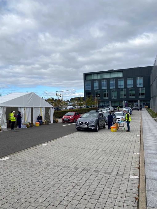 Lines of cars waiting to drive up to a tent and a table where nurses are giving flu jabs to people through the window of their car