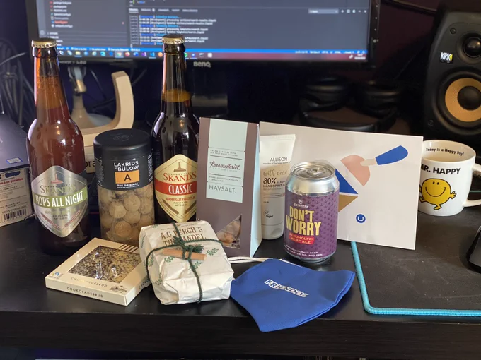 Various bottles of danish beer, some confectionary, danish alcohol get, a blue face mask with friendly written on it and a card from Umbraco displayed on a desk.