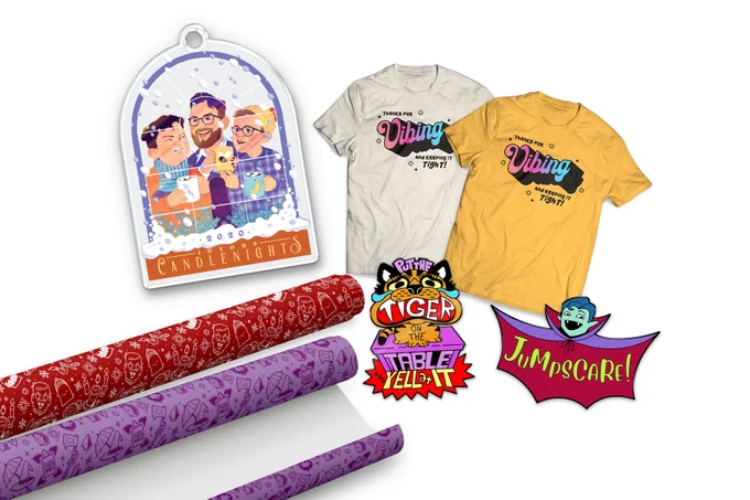 Image of the five October McElroy merch items: an acrylic Candlenights ornament of the brothers in a snowy window, two shirts, one tan, one gold, that say, “Thanks for vibing and keeping it tight!”, an enamel pin of a crying cartoon tiger, an enamel pin of Justin as a vampire that says “Jumpscare!”, a roll of red MBMBaM wrapping paper, and a roll of purple TAZ wrapping paper.