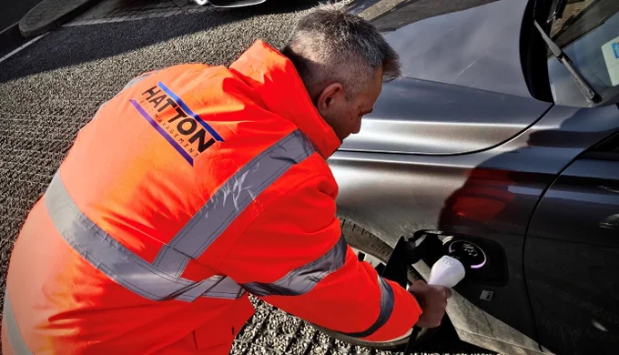 A driver plugs a electric cable into a car.