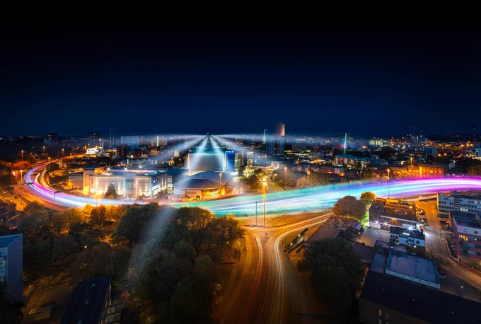 Image: A night-time Coventry skyline with bright colourful lights travelling across the Ring Road.