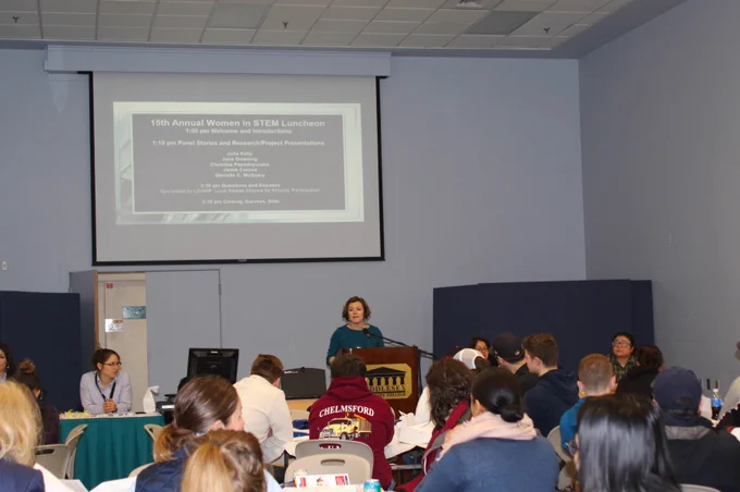 Woman speaks behind a podium to a group of students