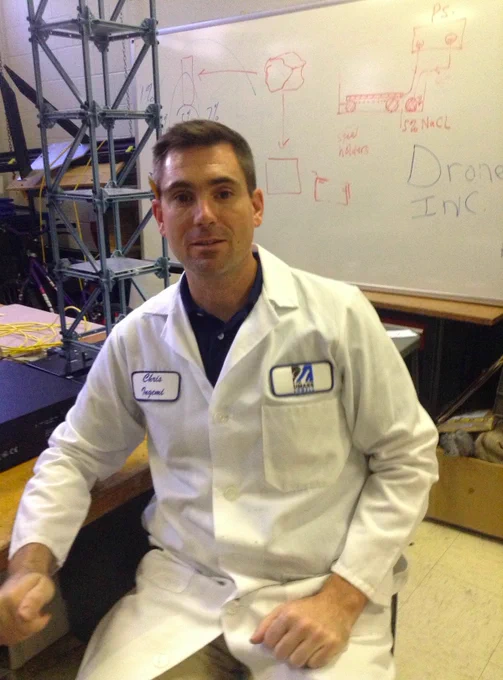 Man wearing lab coat sits at a desk
