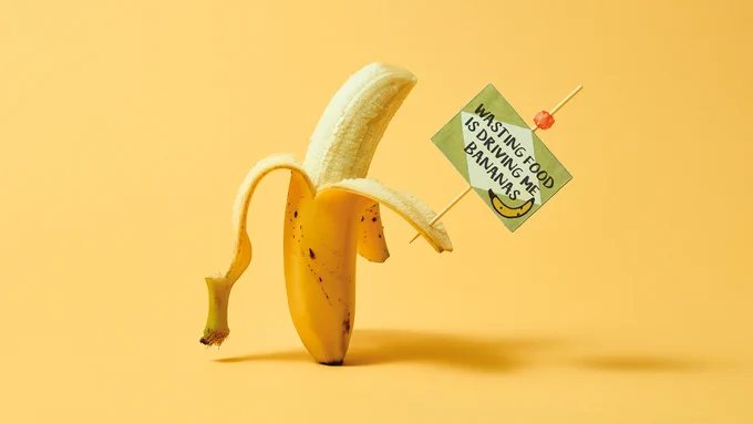 A banana stands with a protest sign which reads "Wasting Food Is Driving Me Bananas"