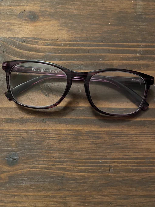 picture of purple glasses sitting on a wooden surface. the brand name "foster grant" is written on the inside of the right temple.