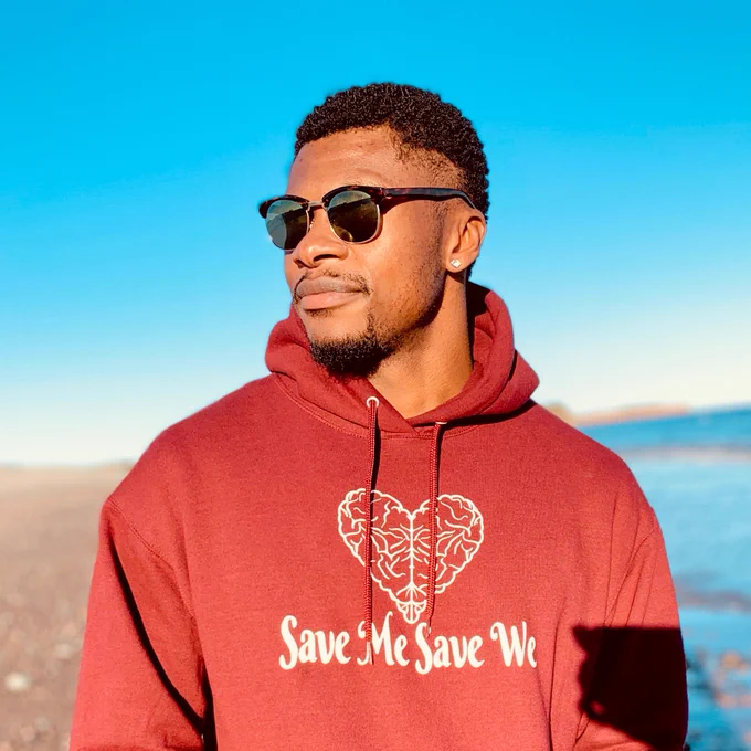 Junior Moaku stands outside wearing a Save Me Save We sweater