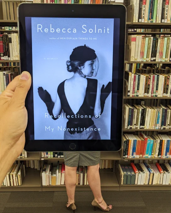 Recollections of My Non-Existence by Rebecca Solnit held in front of a person wearing a skirt and heels. 