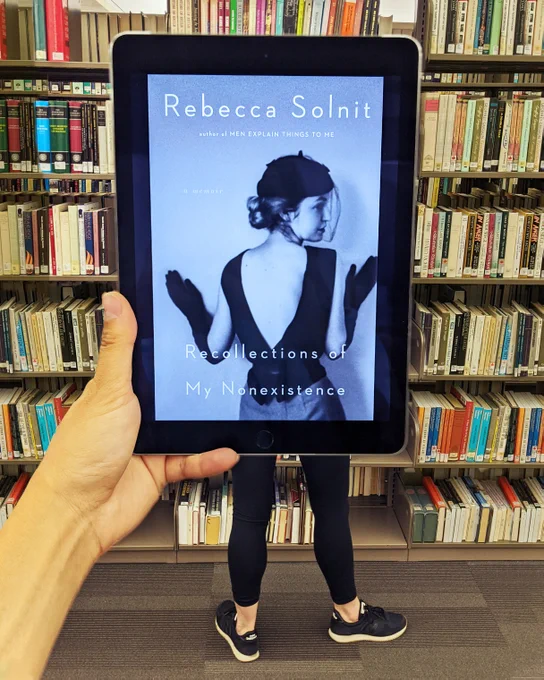 Recollections of My Non-Existence  by Rebecca Solnit ebook held in front of a person wearing leggings and runners. 