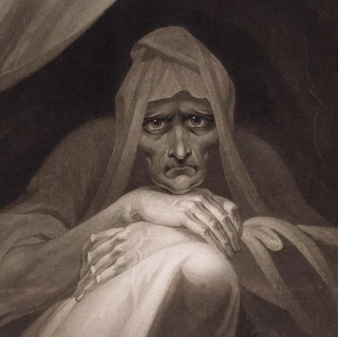 A close up of the same older figure curled up with their knees to their chest and their arms crossed and resting above their knees. The figure wears a billowing garment and  expresses an emotion between sadness, and pensiveness, and stares directly at the viewer.