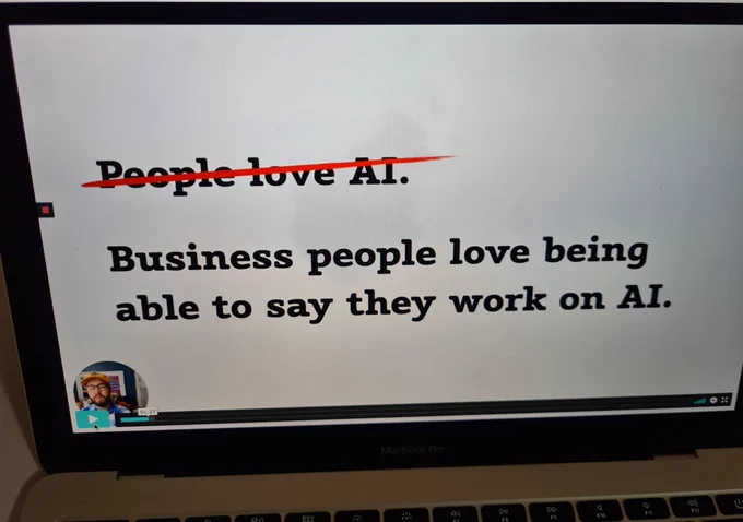 Presentation slide with text that says "People love AI" at the top. This statement has been crossed out in red pen. But underneath it says "Business people love being able to say they work on AI". This text is not crossed out.