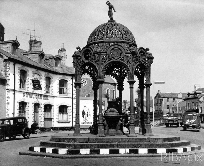 Elaborate cast iron waterfountain in the middle of a street, surrounded by Victorian terraced two-storey houses