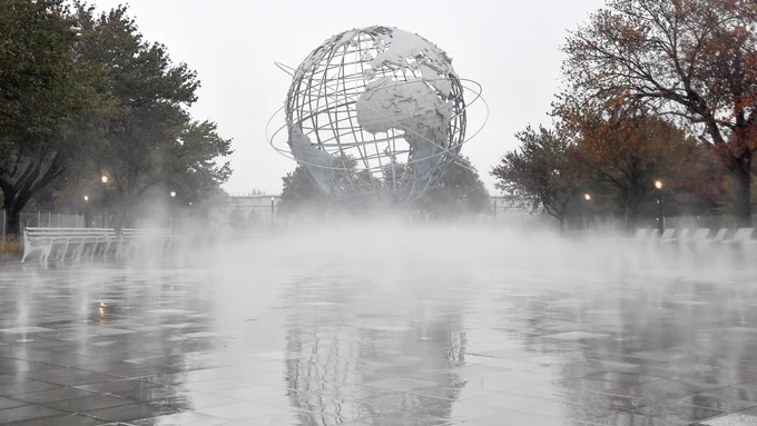 A cloud of mist rises from the new pavement in front of the Unisphere, a giant steel globe, flanked by trees changing into their yellow-red autumn colors.