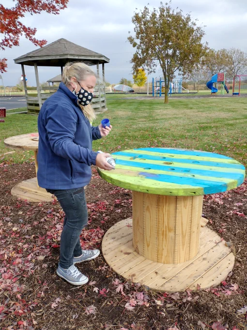 Teacher spray painting wooden spool table green and blue