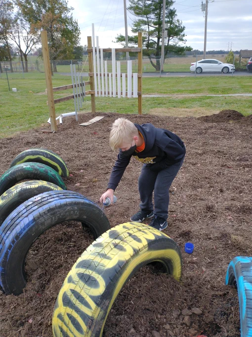 Student spray painting tires in the nature playground
