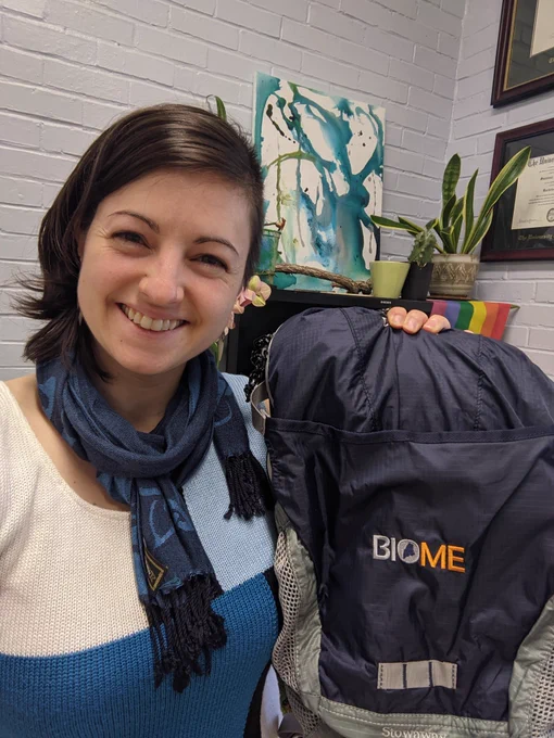 Woman holding up a backpack with "BioME" logo on it.