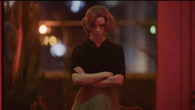 Elizabeth Harmon from The Queen's Gambit, standing dead centre with her arms crossed, looking directly into the camera as she watches, disapproving